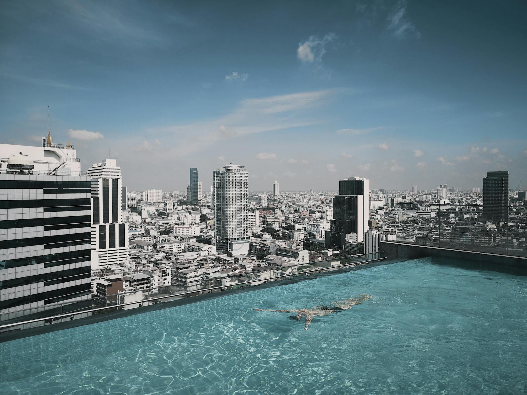 person in swimming pool on top of building facing high rise and mid rise buildings